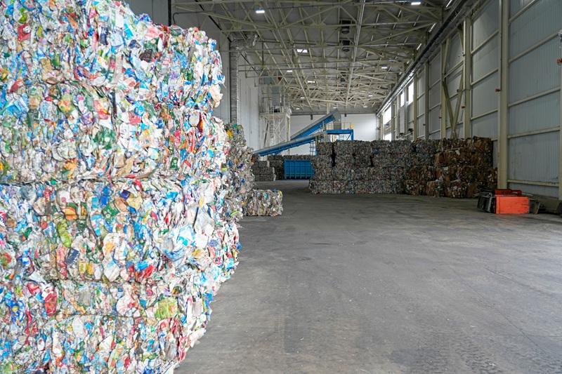 Compressed bales of diverse plastic and paper waste are stacked high inside a vast industrial recycling warehouse, awaiting further material processing Recycling afval bedrijf